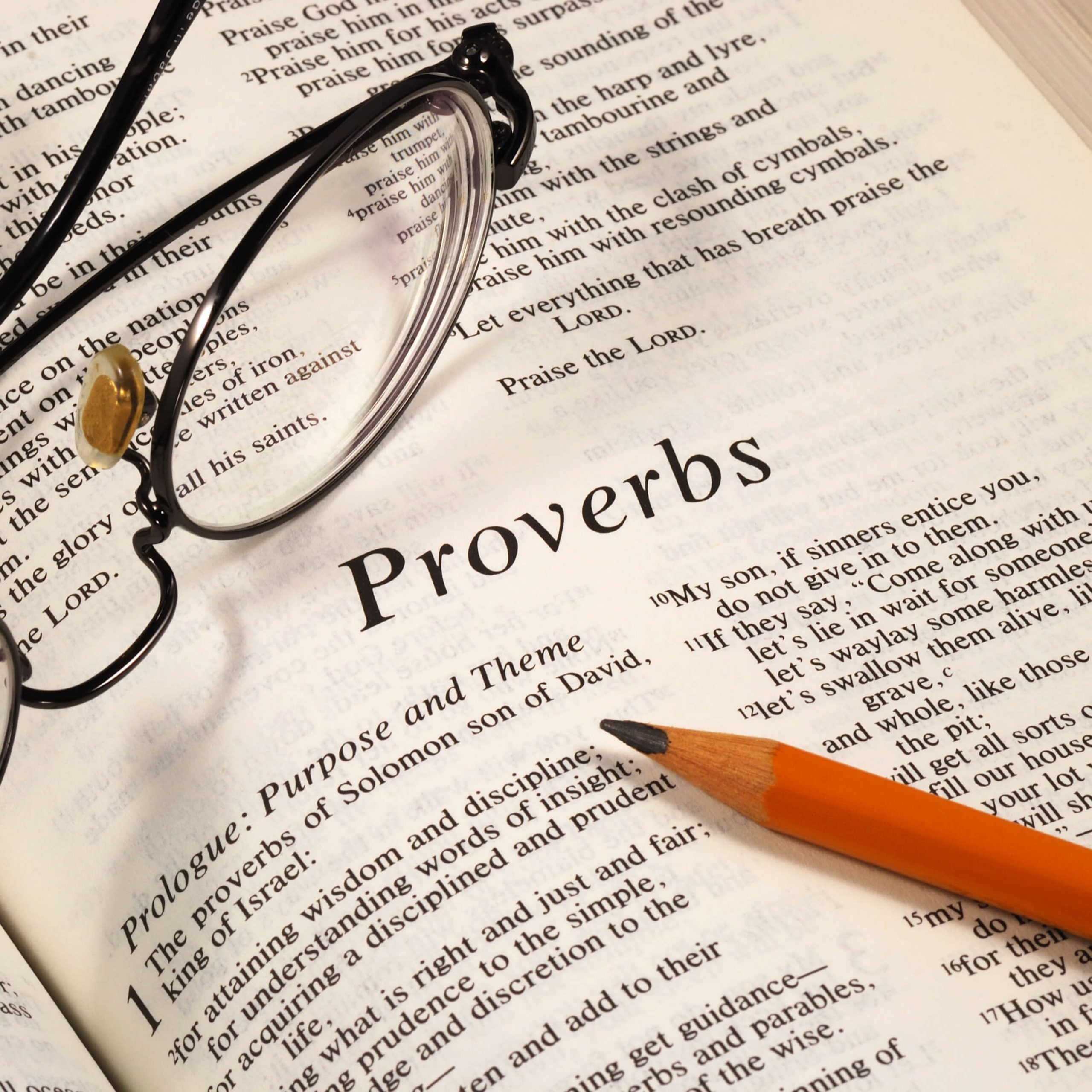 Bible opened to Proverbs with pencil and glasses