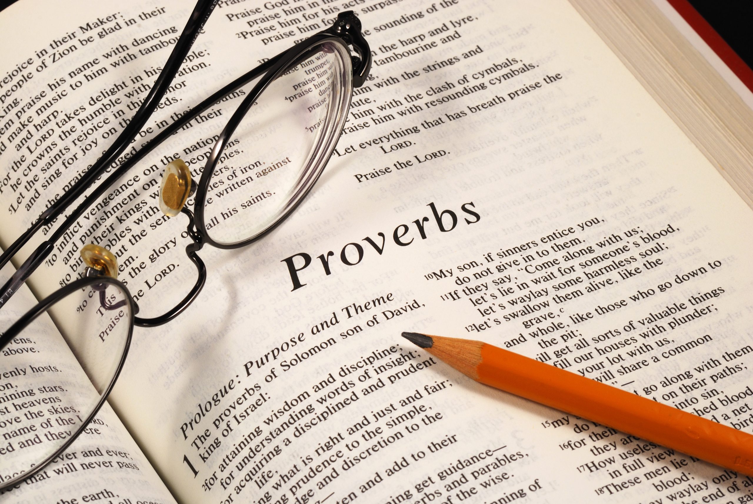 Bible open to Proverbs with pencil and glasses