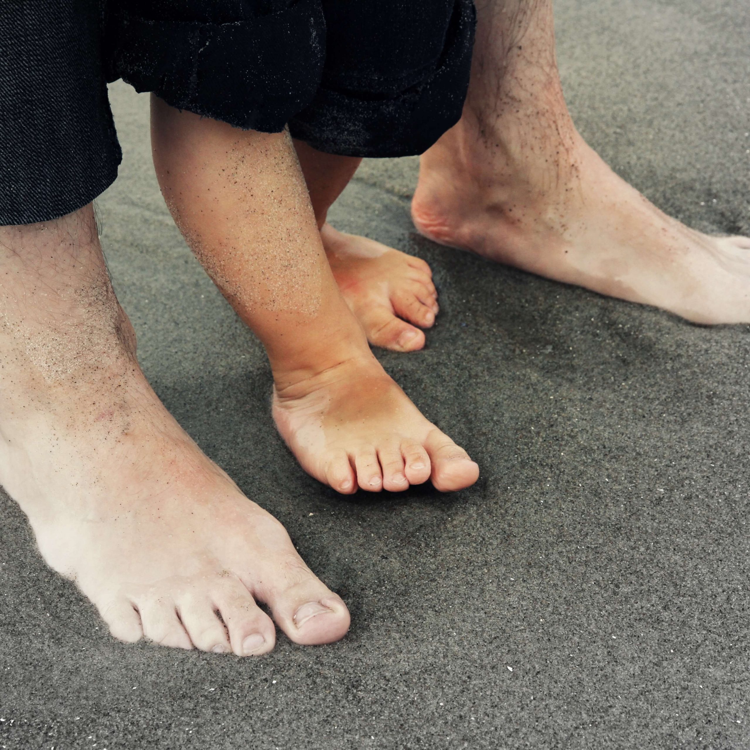man's feet encircling child's feet on sandy beach