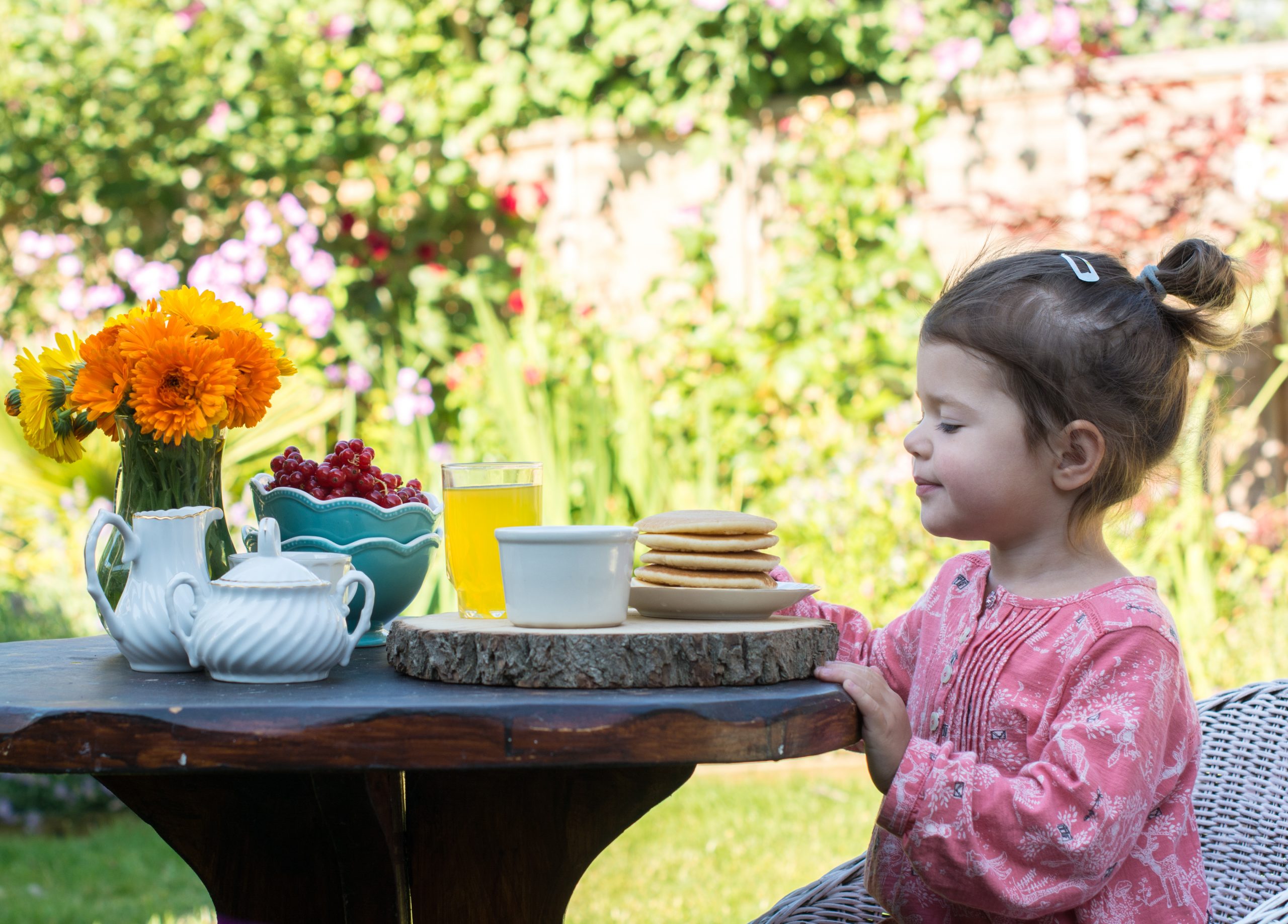girl at table with pancakes in garden