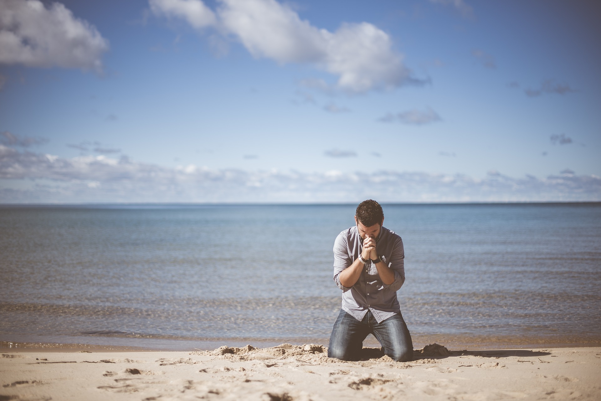 man kneels on beach in prayer